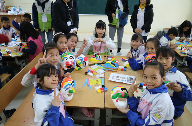 베트남 동로이 초등학생 7명과 한국에서 간 희망봉사단 학생 1명 책상에 앉아 손에 탈을 들고 탈만들기활동을 하고 있는 이미지